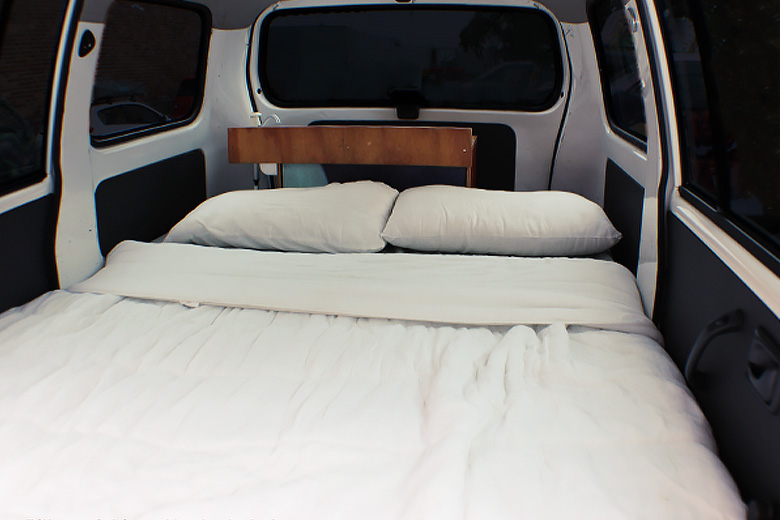 spacious campervan bed made up with white pillows and blankets
